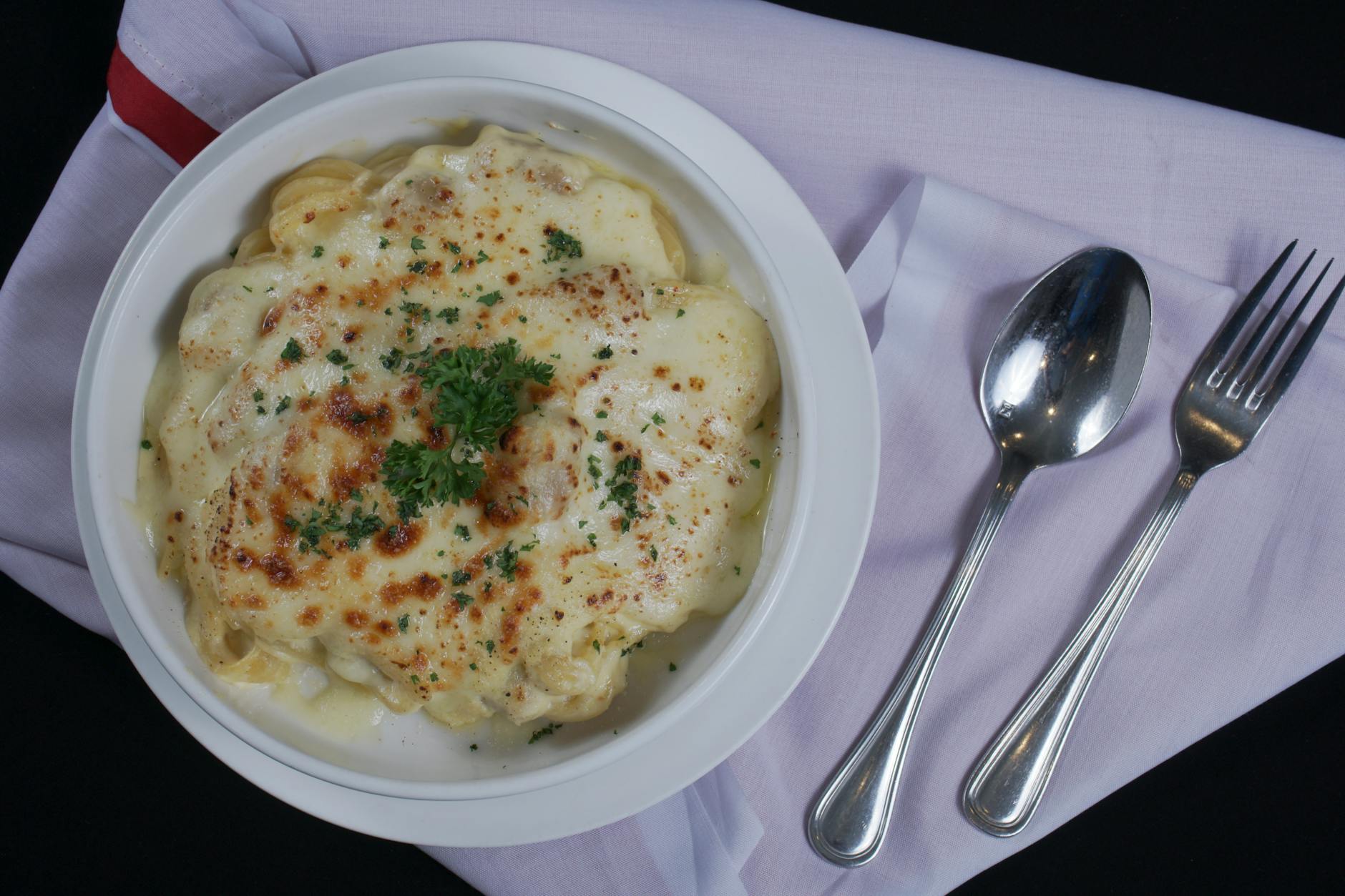 Zapiekany kremowy makaron posypany natką pietruszki na białej serwetce