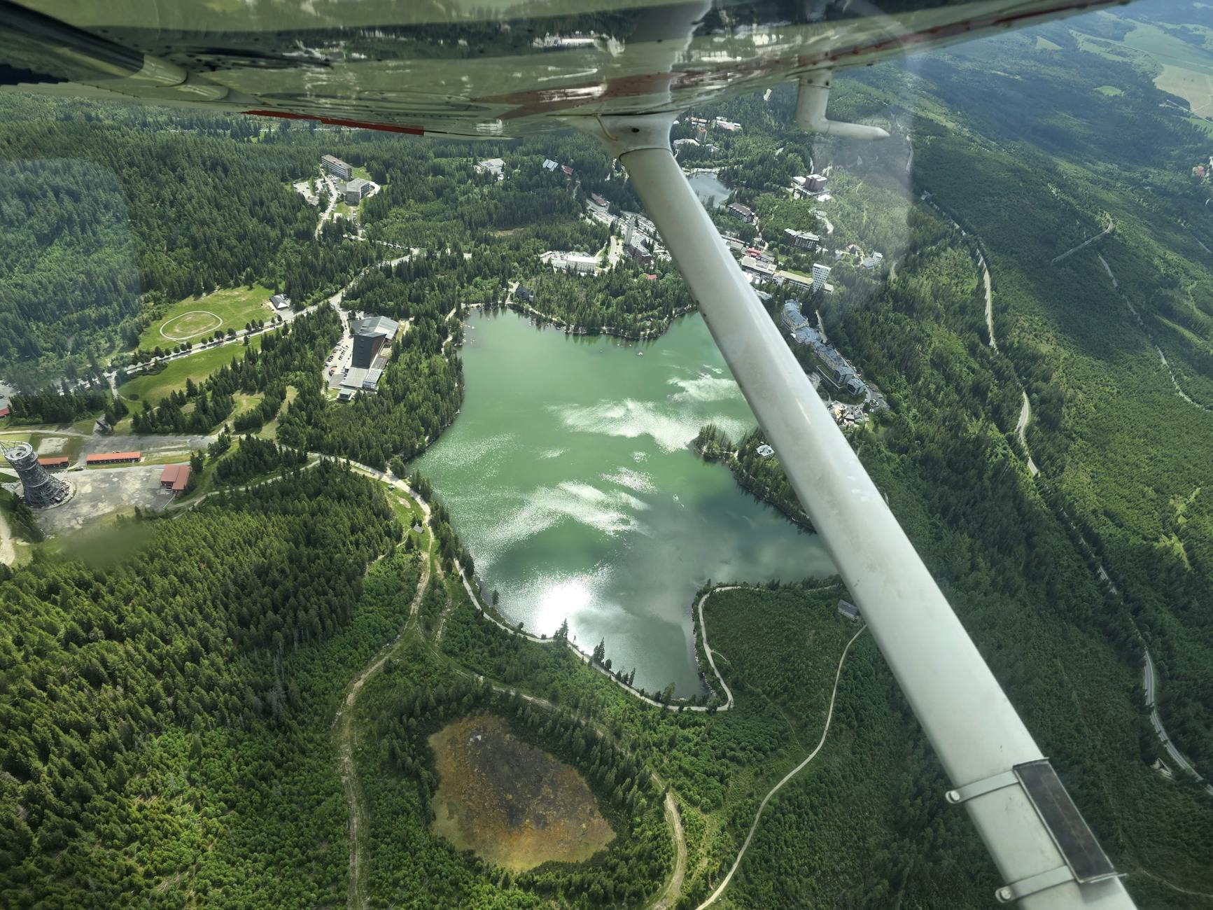 Górskie jezioro otoczone lasem i zabudową z lotu ptaka