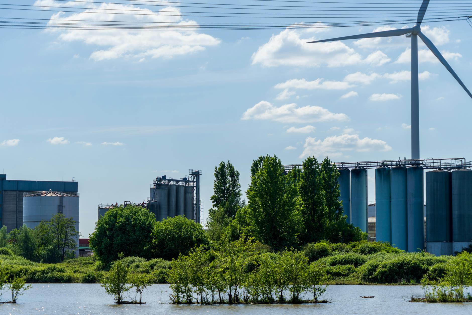Turbina wiatrowa i zakłady przemysłowe nad wodą otoczone zielenią