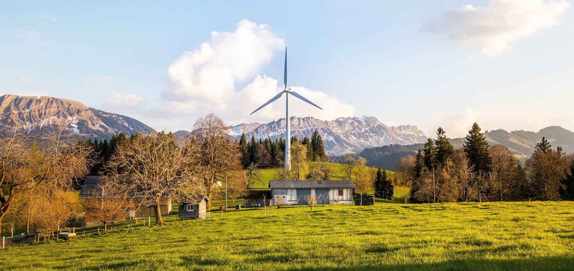 Turbina wiatrowa na zielonych polach z górskim krajobrazem w tle