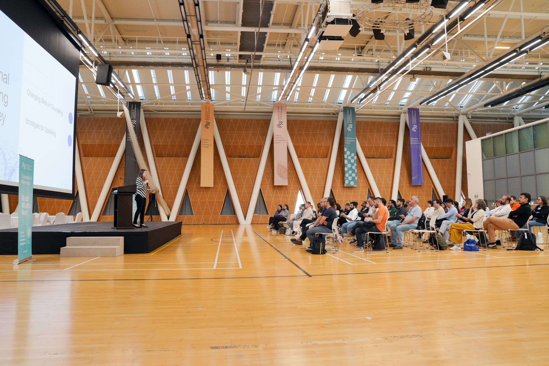 Sala konferencyjna z prelegentem przy mównicy i słuchającą publicznością